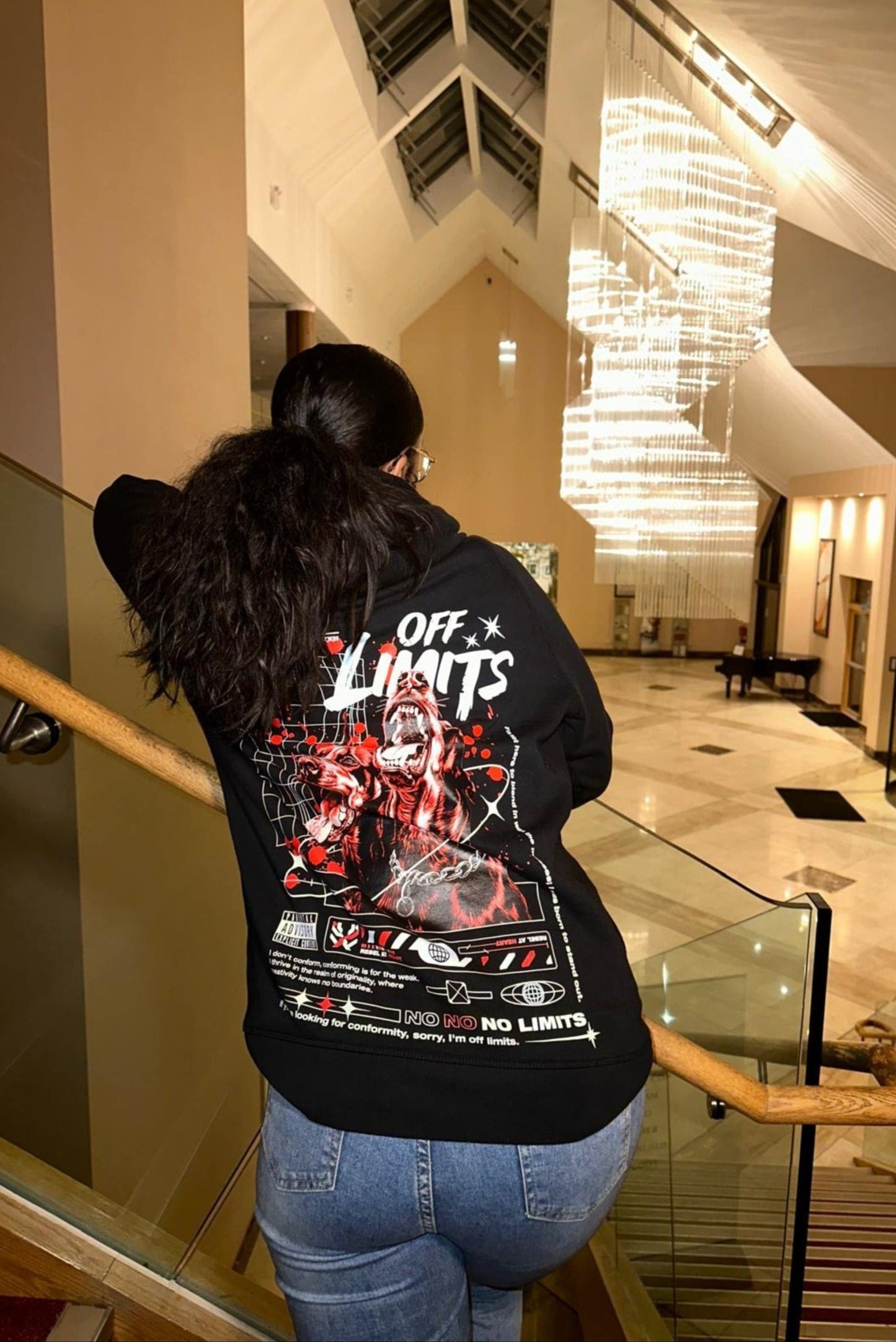 Person wearing a black hoodie with graphic designs and text in an indoor setting