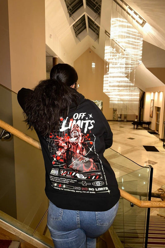 Person wearing a black hoodie with graphic designs and text in an indoor setting